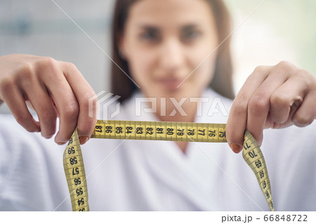 Charming young woman holding yellow tape measure Charming young woman holding yellow tape measure 66848722
