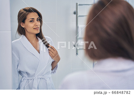 Attractive joyful lady looking in the mirror in bathroom 66848782