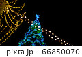 View of Christmas tree decorated large luminous multi-pointed blue stars and yellow balls through garland of yellow lights encircling city square 66850070