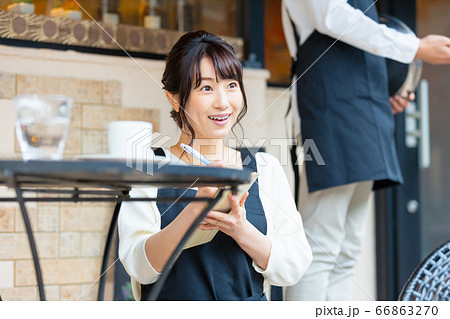 屋外席で客から注文を取る若い飲食店店員女性の写真素材