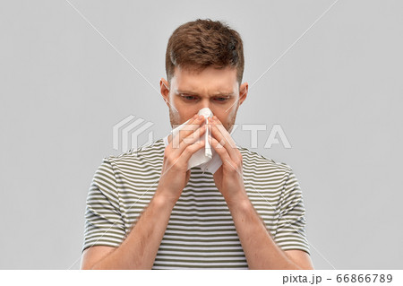 young man with paper tissue blowing his nose young man with paper tissue blowing his nose 66866789