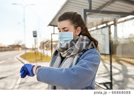 woman in mask looking at wristwatch at bus stop 66868088