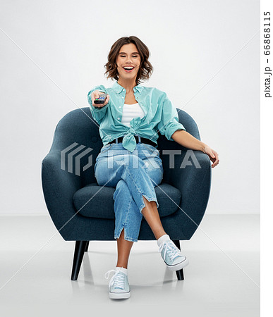 happy woman sitting in armchair with tv remote happy woman sitting in armchair with tv remote 66868115