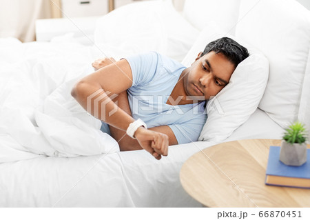 indian man looking at smart watch in bed at home indian man looking at smart watch in bed at home 66870451