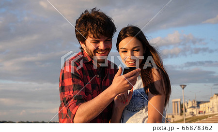 Happy couple watching photos in a smart phone outdoors. Happy couple watching photos in a smart phone outdoors. 66878362