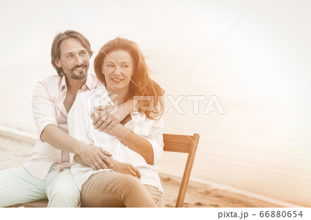 Happy mature couple hugs sitting in beach cafe at sea side. Portrait of hugging pretty two people in love with copy space at right side. Tinted image 66880654