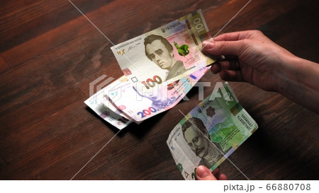 Mans hands counting Ukrainian hryvna or hryvnia money. Man holding pack of new Ukrainian banknotes, at wooden table background. Cash money concept. Investment concept. Close up shot Mans hands counting Ukrainian hryvna or hryvnia money. Man holding pack of new Ukrainian banknotes, at wooden table background. Cash money concept. Investment concept. Close up shot 66880708