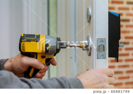 Handyman using a drill to installing lock in door Handyman using a drill to installing lock in door 66883799