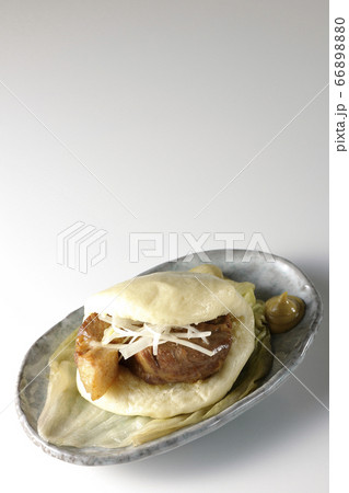 レタスが敷いてあるお皿に置かれた白髪ねぎも一緒に挟まったシンプルな角煮まんと和がらし（白背景） 66898880