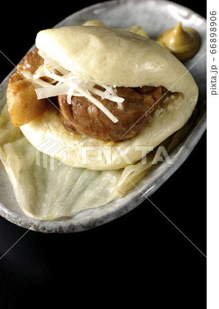 レタスが敷いてあるお皿に置かれた白髪ねぎも一緒に挟まったシンプルな角煮まんと和がらし（黒背景） 66898906