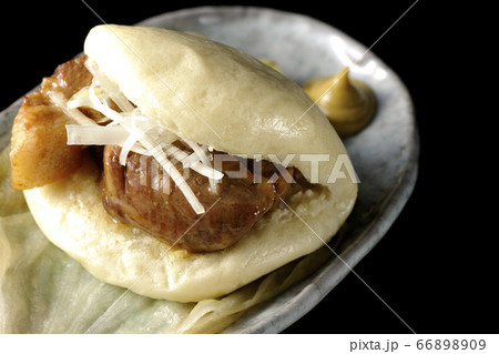 レタスが敷いてあるお皿に置かれた白髪ねぎも一緒に挟まったシンプルな角煮まんと和がらし（黒背景） 66898909