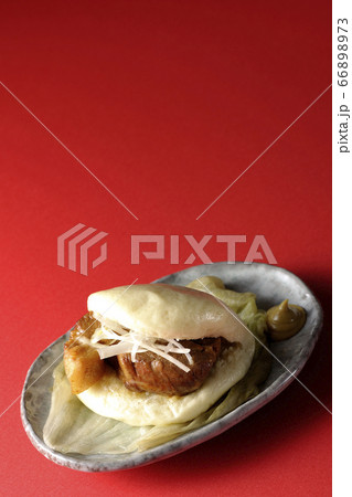 レタスが敷いてあるお皿に置かれた白髪ねぎも一緒に挟まったシンプルな角煮まんと和がらし 66898973