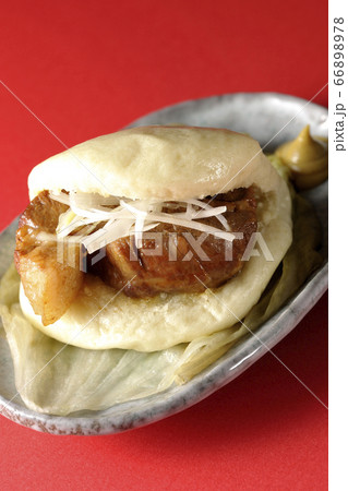 レタスが敷いてあるお皿に置かれた白髪ねぎも一緒に挟まったシンプルな角煮まんと和がらし 66898978