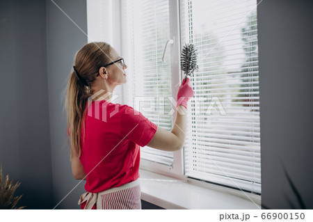 Woman using hand held duster for cleaning window shutters Woman using hand held duster for cleaning window shutters 66900150