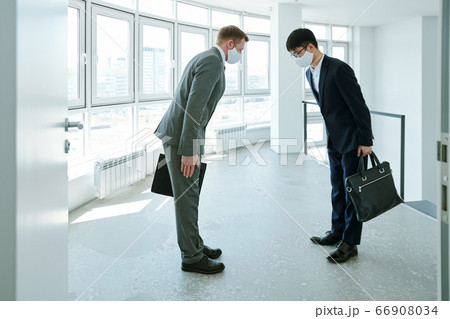 Elegant intercultural businessmen with briefcases greeting each other by bow Elegant intercultural businessmen with briefcases greeting each other by bow 66908034