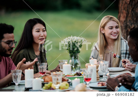 Young intercultural females talking to their boyfriends by served table outdoors Young intercultural females talking to their boyfriends by served table outdoors 66908182