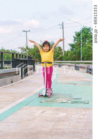 Little child girl to ride scooter in outdoor sports ground on sunny summer day 66915353