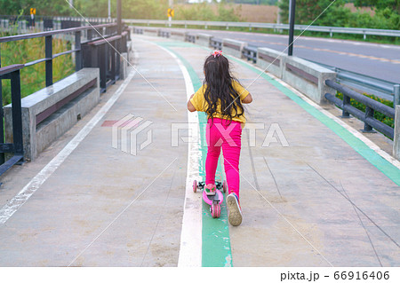 Little child girl to ride scooter in outdoor sports ground on sunny summer day 66916406