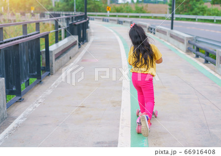 Little child girl to ride scooter in outdoor sports ground on sunny summer day Little child girl to ride scooter in outdoor sports ground on sunny summer day 66916408