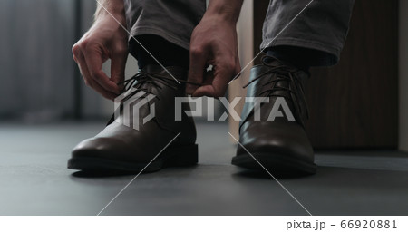 Young man put on his brown leather chukka boots indoor 66920881