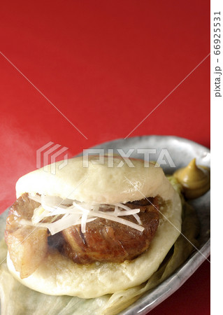 レタスが敷いてあるお皿に置かれた白髪ねぎも一緒に挟まった蒸したてで湯気上がる熱々な角煮まんと和がらし 66925531