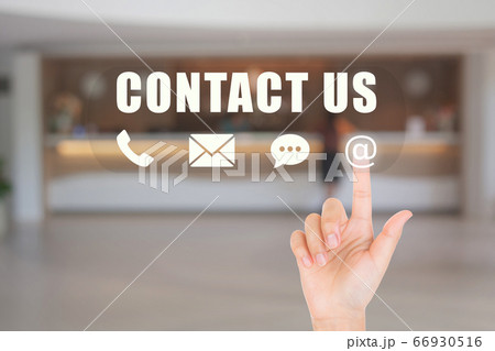 Hand choosing and pressing on contact us icon symbols with blurry image of luxury hotel lobby reception in the background. 66930516