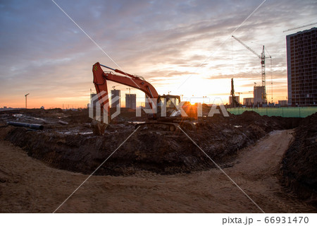 Red excavator at building under construction against the background sunset Red excavator at building under construction against the background sunset 66931470