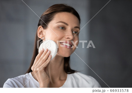 Smiling female look in mirror do facial skincare procedures Smiling female look in mirror do facial skincare procedures 66933578