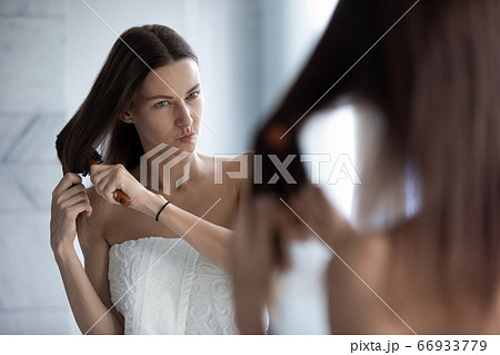 Unhappy woman brush tangled long hair in bathroom Unhappy woman brush tangled long hair in bathroom 66933779