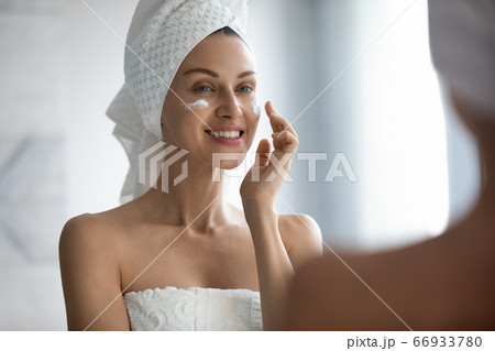 Young lady look in mirror use facial lotion in morning Young lady look in mirror use facial lotion in morning 66933780
