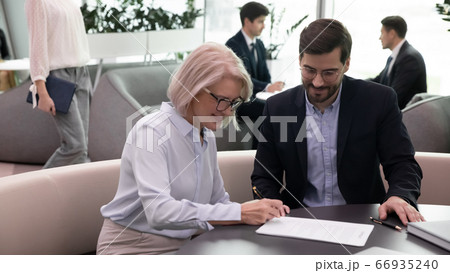 Happy middle aged woman signing document meeting with broker, insurer Happy middle aged woman signing document meeting with broker, insurer 66935240
