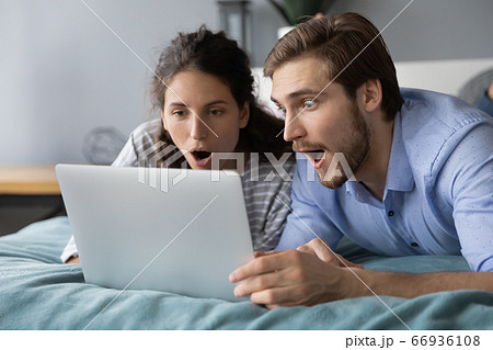 Shocked young couple looking at laptop screen, lying on bed Shocked young couple looking at laptop screen, lying on bed 66936108