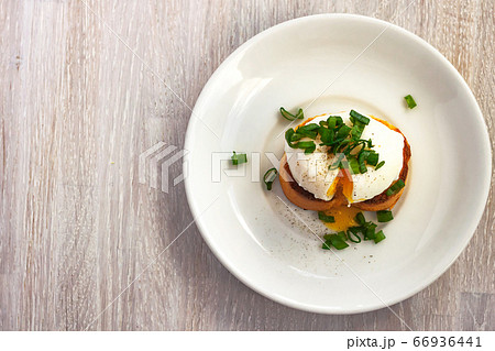 Poached egg, liquid yolk with, green onion on toast bread, white plate on white wooden background Poached egg, liquid yolk with, green onion on toast bread, white plate on white wooden background 66936441