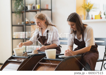 Overview of two young potters by pottery wheels while preparing ceramic pots from raw clay. 66937515