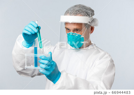 Covid-19, preventing virus, healthcare workers and vaccination concept. Tech lab doctor in clinic wearing personal protective equipment working over vaccine, looking at test-tubes samples 66944483