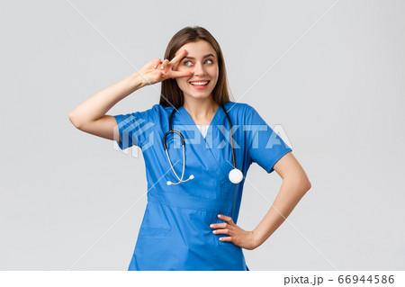 Medical workers, healthcare, covid-19 and vaccination concept. Cheerful and energized young female doctor, pretty nurse in blue scrubs, stethoscope, show peace near eye and smiling upbeat 66944586