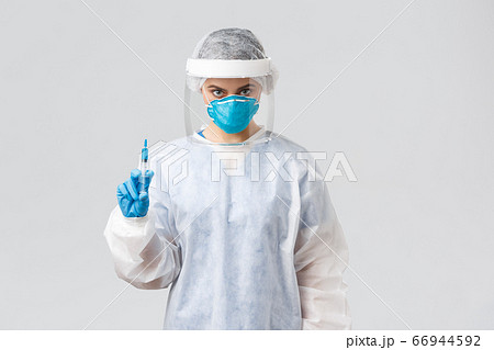 Covid-19, medical research, diagnosis, healthcare workers and quarantine concept. Serious doctor or nurse in personal protective equipment, face shield holding syringe with coronavirus vaccine 66944592