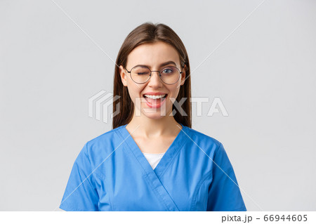 Healthcare workers, medicine, insurance and covid-19 pandemic concept. Cheeky pretty female nurse, intern or doctor in clinic, wear scrubs and glasses, wink at camera with enthusiastic smile 66944605