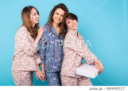 Portrait of three beautiful young girls wearing colorful pyjamas having fun during sleepover isolated over blue background. Pajama party and hen-party concept 66949527