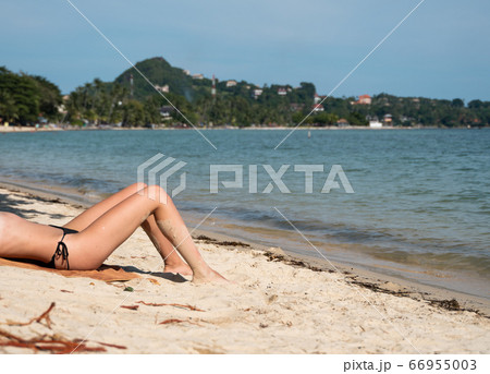 Beautiful slim women's legs on the beach. Lower half of the girl body lying on the beach by the sea. Young women's wet and sun-tanned legs on the beach with the sea view. 66955003