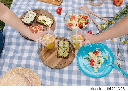 Photo of two hand hold orange lemonade in front of vegan picnic outdoors. Healthy food concept Photo of two hand hold orange lemonade in front of vegan picnic outdoors. Healthy food concept 66961368