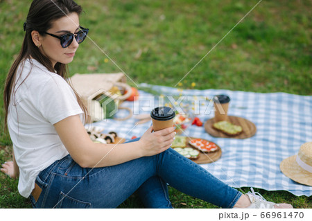 Close-up of woman hold disposable cup with coffee on picnic outdoors. Space for text. Vegan picnic concept Close-up of woman hold disposable cup with coffee on picnic outdoors. Space for text. Vegan picnic concept 66961470