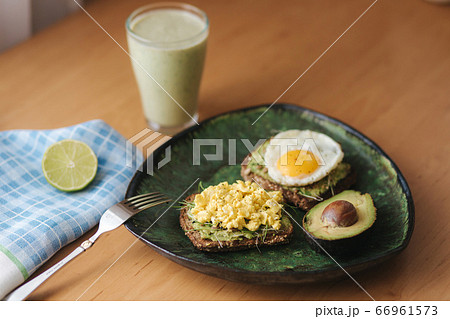 Different cooked egg on avocado sandwich with whole grain bread on wooden board. Smoothie with spinach 66961573