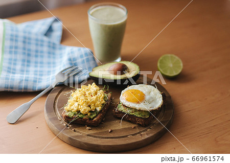 Different cooked egg on avocado sandwich with whole grain bread on wooden board. Smoothie with spinach 66961574