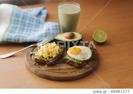 Different cooked egg on avocado sandwich with whole grain bread on wooden board. Smoothie with spinach 66961577