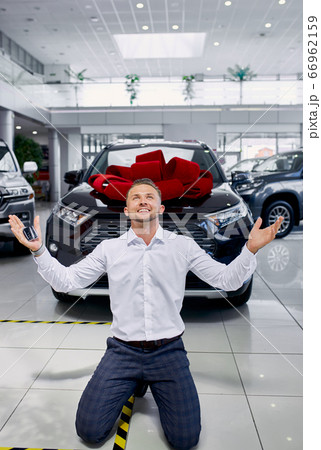 happy handsome caucasian man standing on his knees in front of his newly bought cool car 66962159