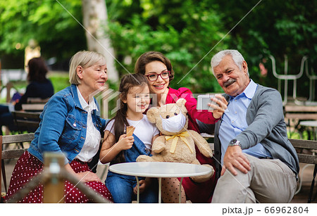 Senior couple with daughter and granddaughter sitting outdoors in cafe, taking selfie. 66962804