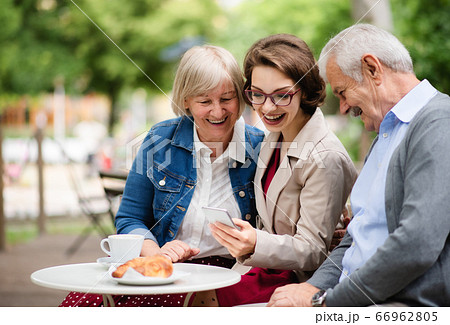 Woman with senior parents sitting outdoors in cafe, using smartphone. 66962805