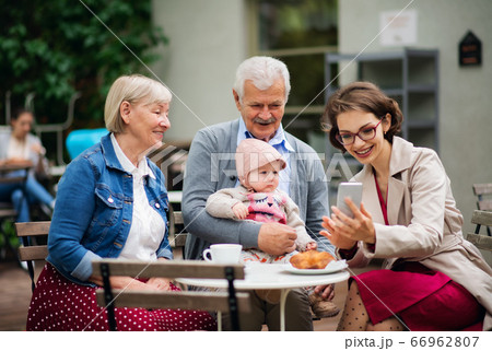Senior couple with daughter and baby granddaughter sitting outdoors in cafe. 66962807