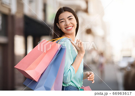 Smiling asian woman carrying shopping bags outdoors and posing to camera 66963617